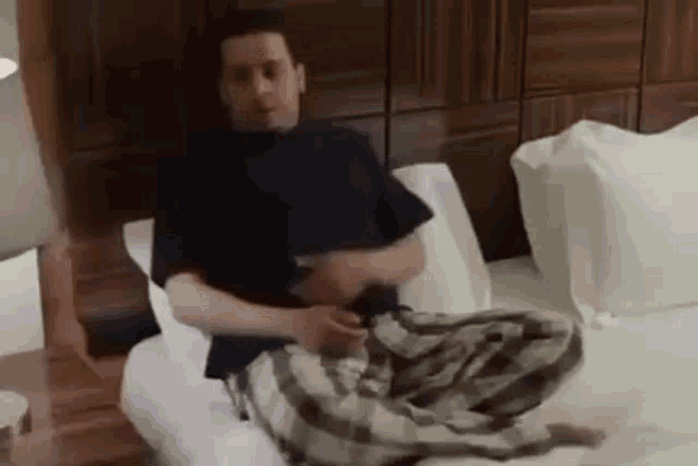 a man is sitting on a bed with a blanket on his stomach and playing a guitar .
