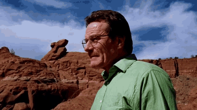 a man wearing glasses and a green shirt stands in front of a desert landscape