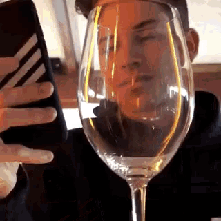 a man is taking a picture of himself with a wine glass in front of his face .