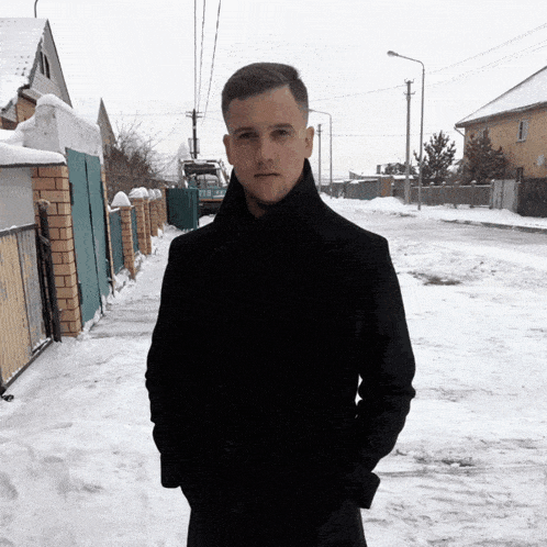 a man in a black coat is standing in the snow with his hands in his pockets