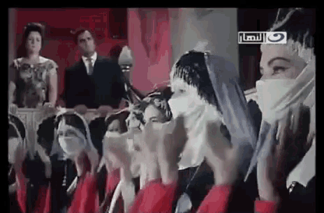 a group of people wearing face masks are clapping their hands in a room .