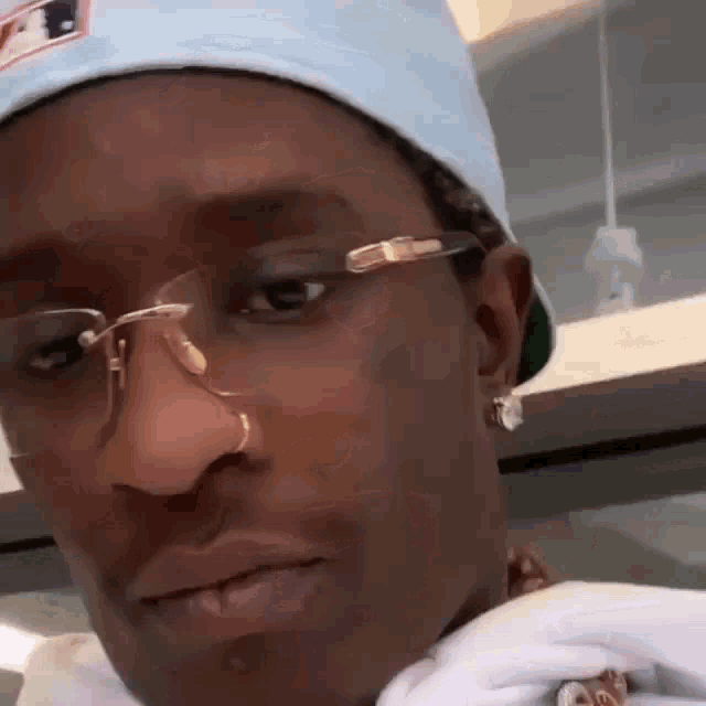 a close up of a man wearing glasses , a nose ring , and a hat .