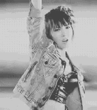 a black and white photo of a woman in a denim jacket holding her arm in the air .