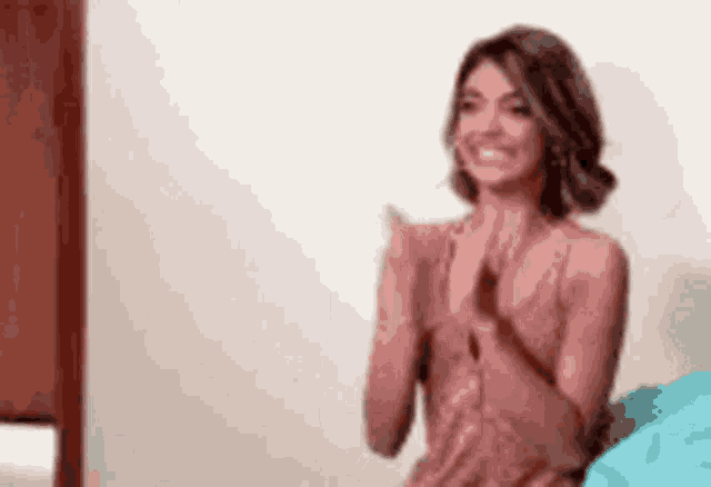 a woman in a pink dress is sitting on a bed clapping her hands .
