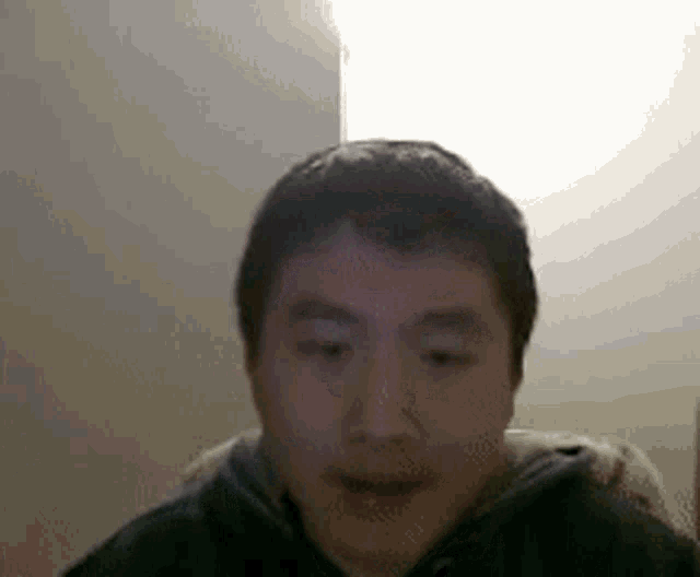 a man in a black hoodie is sitting in front of a white wall .