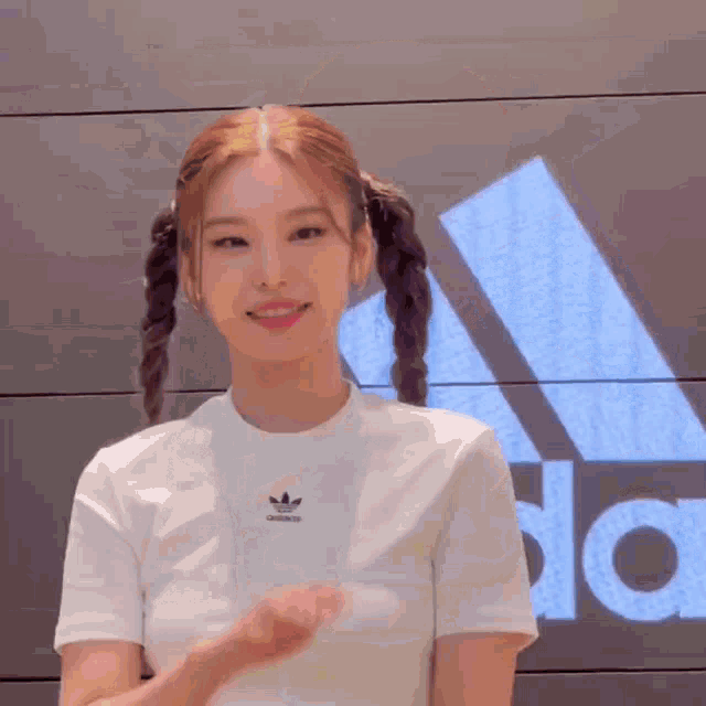a woman wearing a white adidas t-shirt is standing in front of an adidas sign .