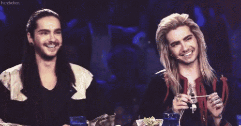 two men with long hair are sitting at a table laughing