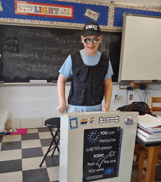 a boy in a swat uniform stands in front of a podium in a classroom