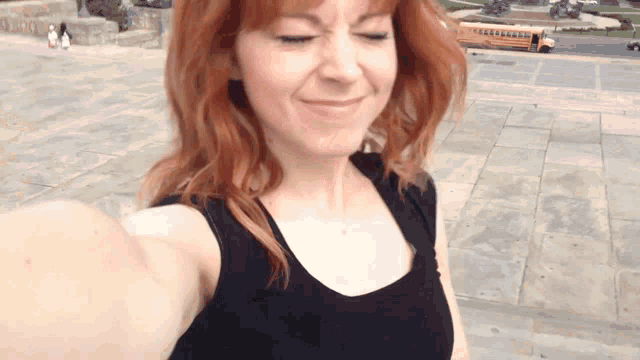 a woman with red hair is taking a selfie with a yellow school bus in the background