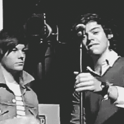 a black and white photo of two men singing into microphones .