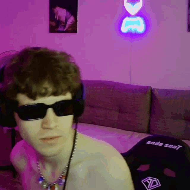 a shirtless man wearing sunglasses and headphones is sitting in front of a purple wall with a neon sign that says dc