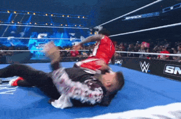 a man in a red shirt is wrestling another man in a blue ring