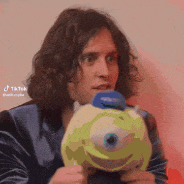 a man with long hair is holding a stuffed mike from monsters inc.