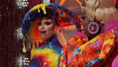 two drag queens are standing next to each other and one is wearing a colorful outfit