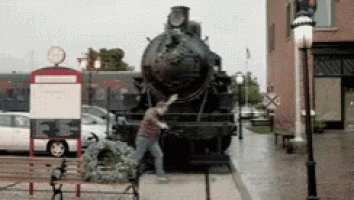 a man is standing in front of a train with a wreath on the ground in front of it