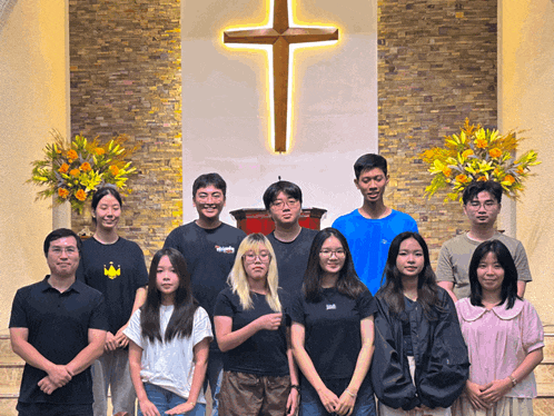 a group of people pose in front of a cross
