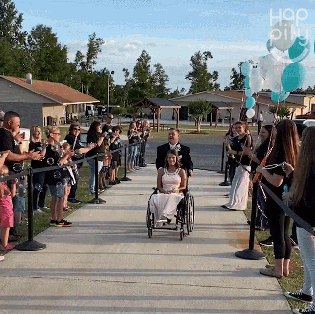 a woman in a wheelchair is walking down a sidewalk surrounded by people and balloons with the word hap on the bottom