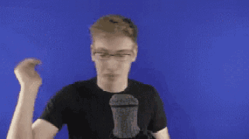 a young man wearing glasses and a black shirt is standing in front of a blue screen .