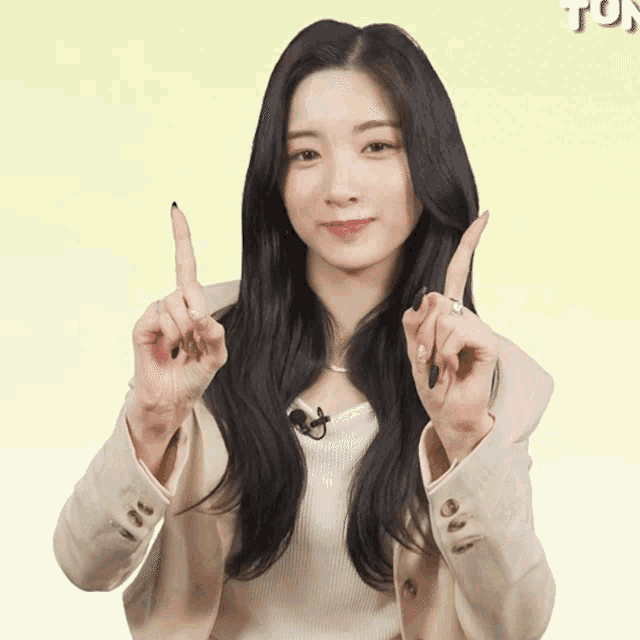 a woman with long black hair and a tan jacket is giving a thumbs up