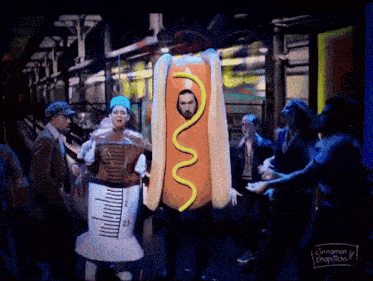 a man dressed as a hot dog with mustard on it is surrounded by people