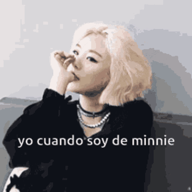 a woman with blonde hair is sitting on a couch with her hand on her nose and the words yo cuando soy de minnie above her .
