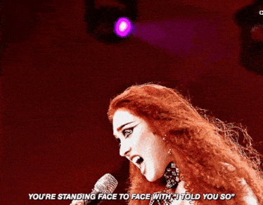 a woman singing into a microphone with the words " you 're standing face to face with i told you so " below her