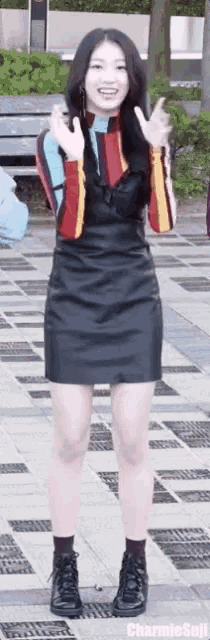 a woman in a black dress is standing on a sidewalk and making a peace sign .