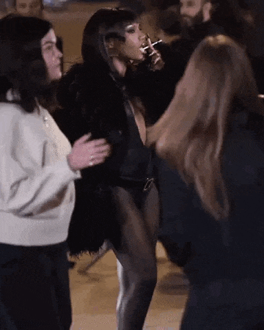 a woman in a black bodysuit is smoking a cigarette while dancing in a crowd of people .