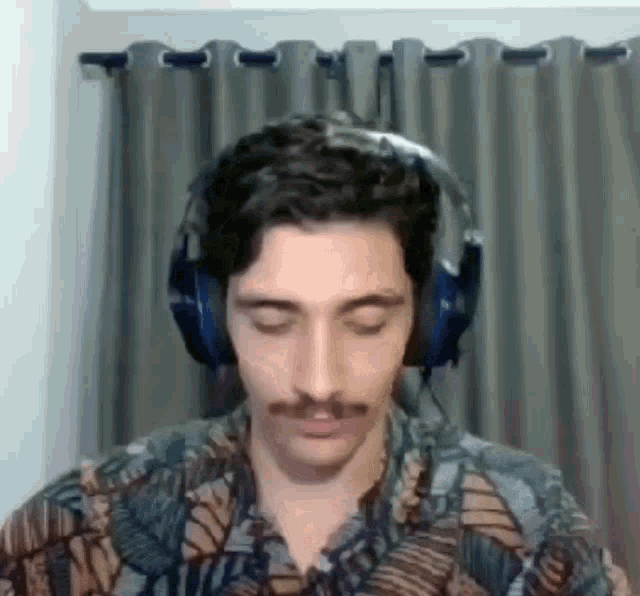a man with a mustache is wearing headphones and a floral shirt .
