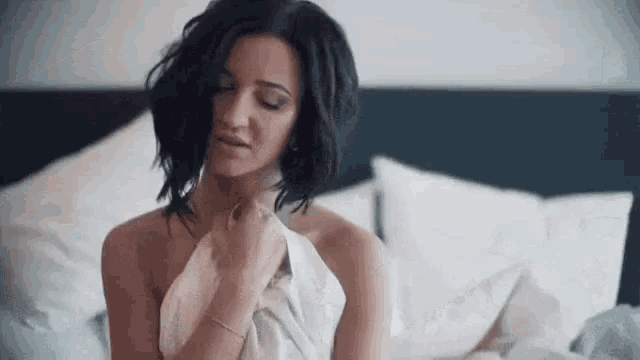 a naked woman is sitting on a bed wrapped in a white sheet .