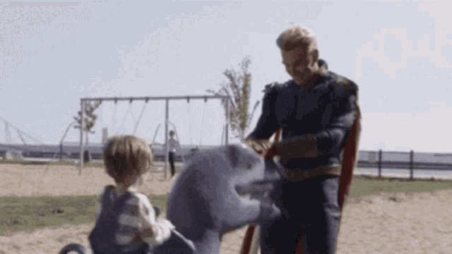 a man in a superhero costume is playing with a toy shark and a little boy in a playground .