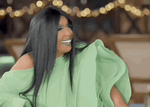 a woman with long black hair is wearing a green off the shoulder top