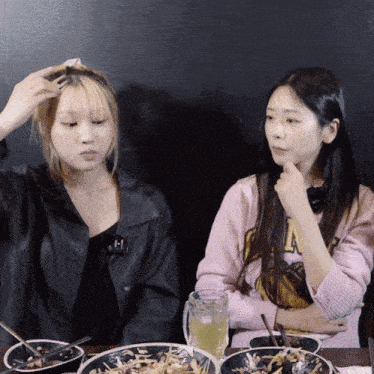 a woman in a pink sweater with the letter a on it sits next to another woman in a black jacket