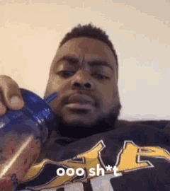 a man is sitting on a couch drinking from a water bottle and making a funny face .