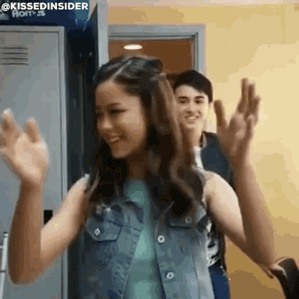 a girl in a denim vest is dancing in a locker room with a boy .