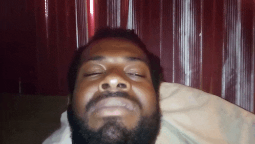 a man with a beard is laying on a pillow with his eyes closed