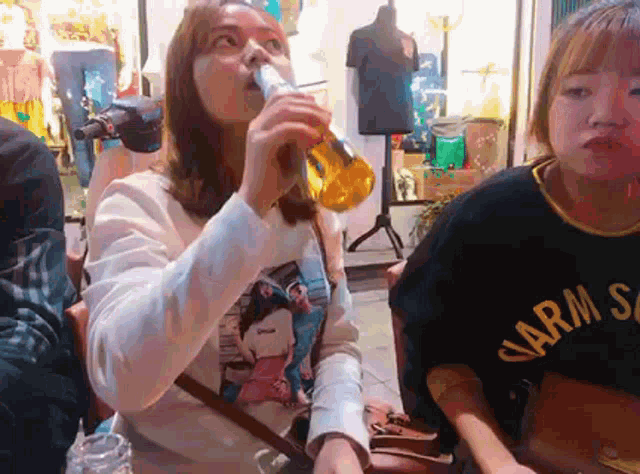 a woman drinking from a bottle while wearing a shirt that says arms