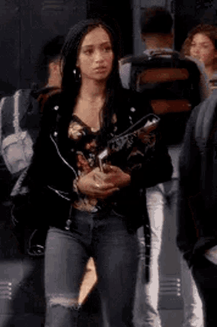 a woman in a leather jacket and jeans is standing in a locker room holding a guitar .