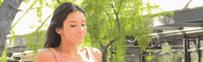 a woman is standing in front of a tree looking down .