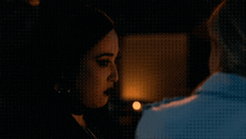 a man and a woman looking at each other in a dark room