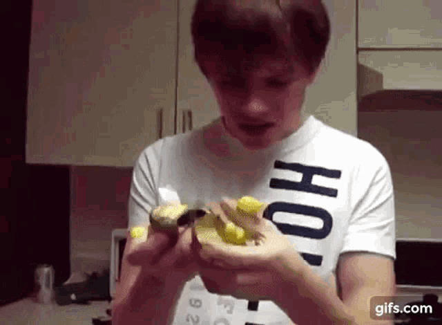 a man wearing a white shirt with the word ho on it is peeling a banana .
