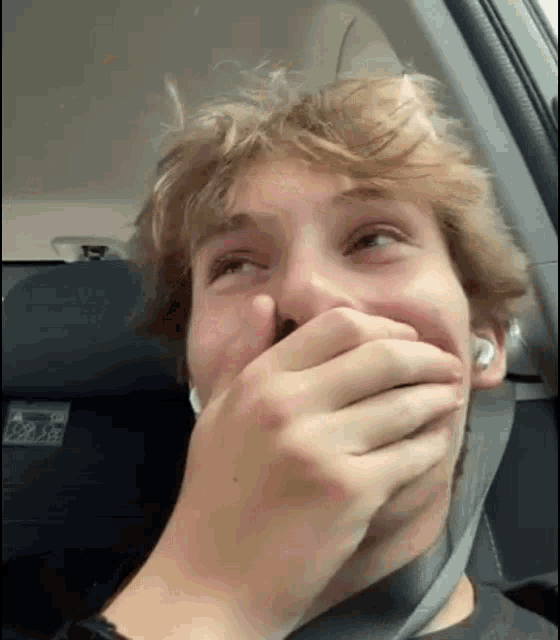 a young man in a car is covering his mouth with his hand .
