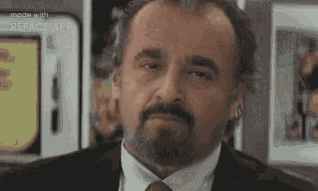 a man with a beard and mustache is wearing a suit and tie and looking at the camera .