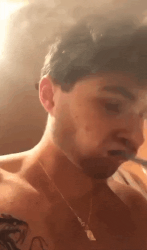 a shirtless man with a tattoo on his chest is taking a selfie with his phone .