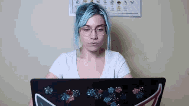 a woman with blue hair and glasses is looking at a laptop