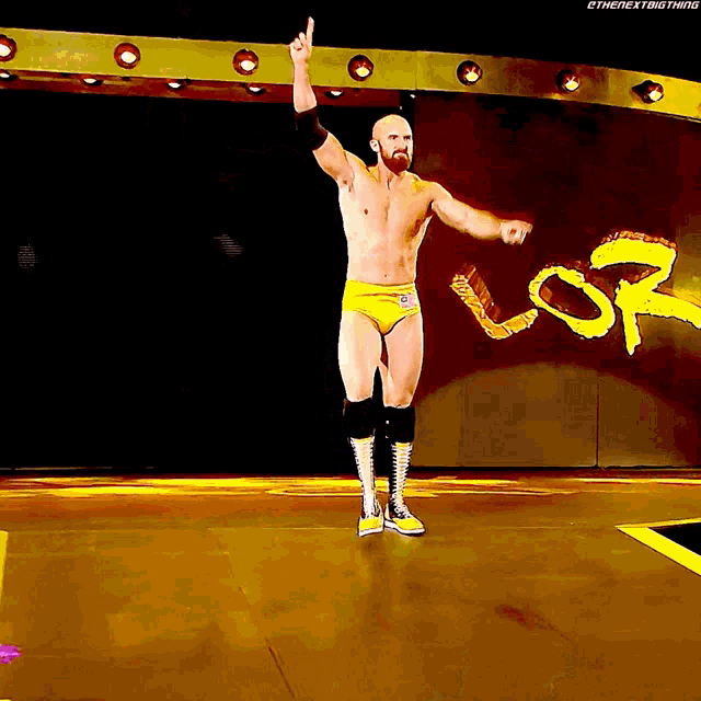 a shirtless wrestler in yellow shorts is standing in front of a sign that says sr