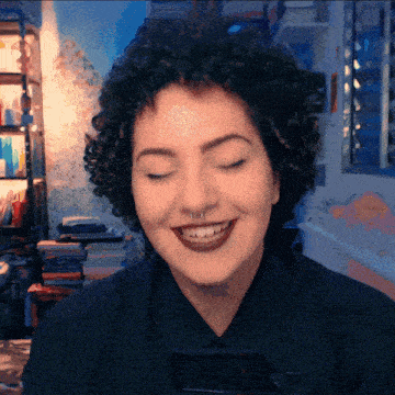 a woman with curly hair and a nose ring smiles