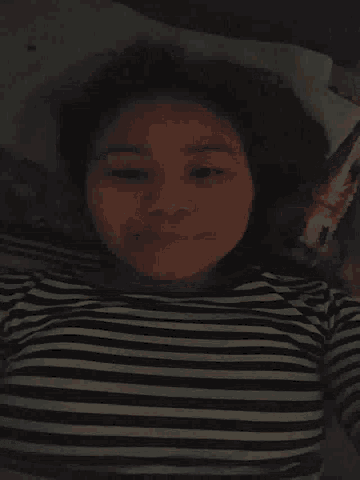 a woman in a black and white striped shirt is laying on a bed and smiling .