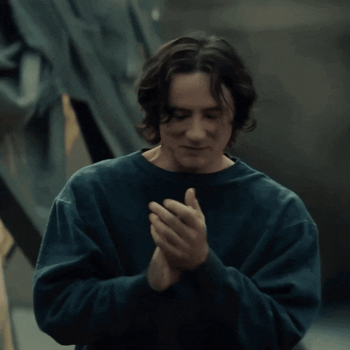 a man in a blue sweatshirt is clapping his hands together