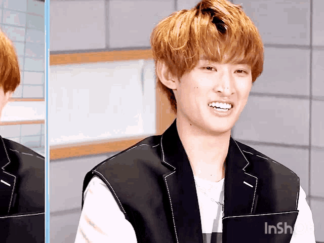 a man with blonde hair is smiling and wearing a black vest that says inshot